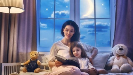 Une maman et son enfant sont assis sur un lit et lisent un livre