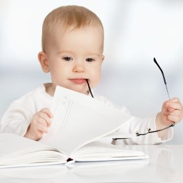 photo d'un bébé avec un livre a la main et des lunettes a la bouche